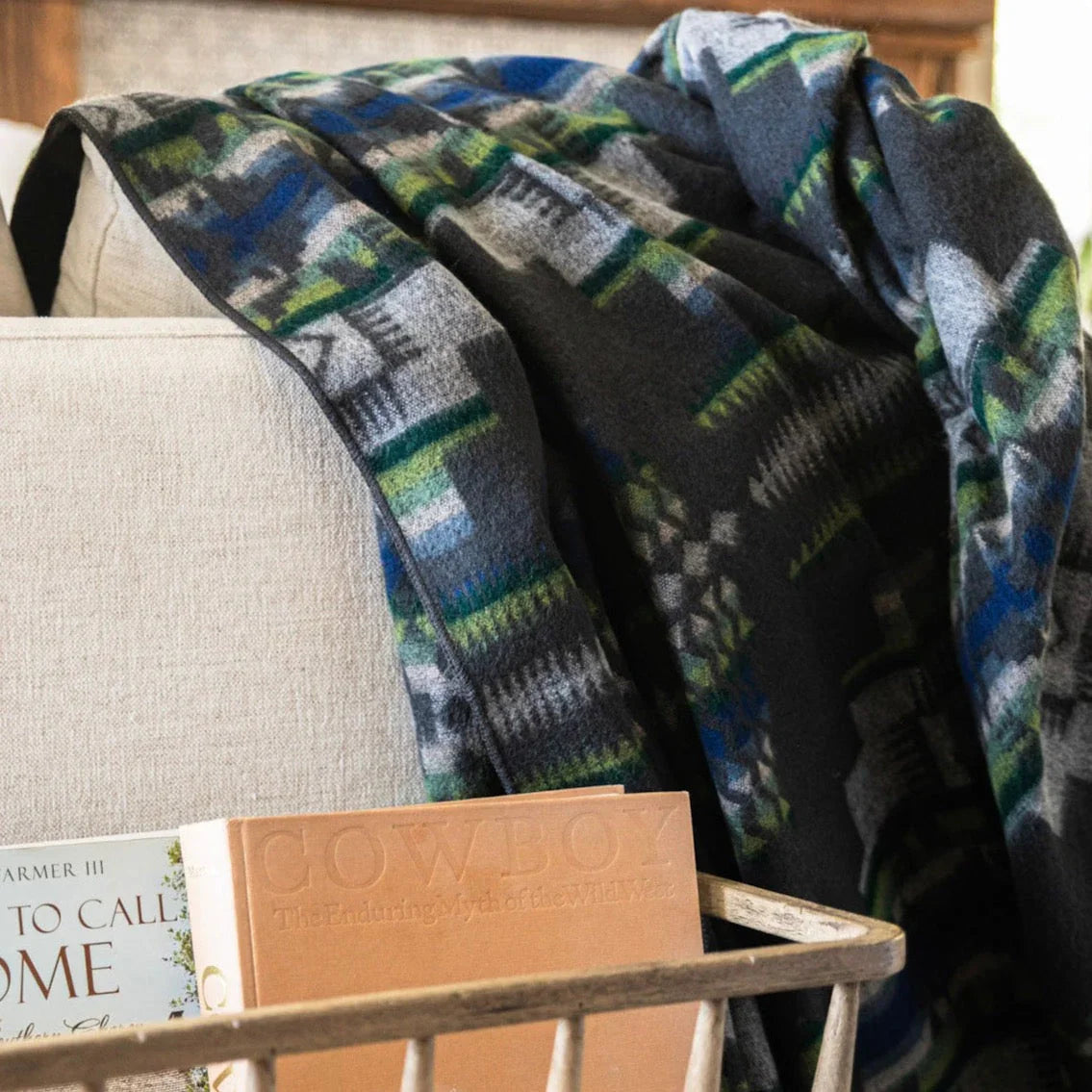 A Southwestern patterned blanket in shades of blue and black draped over the back of a chair, with a book on a table beside it - Your Western Decor