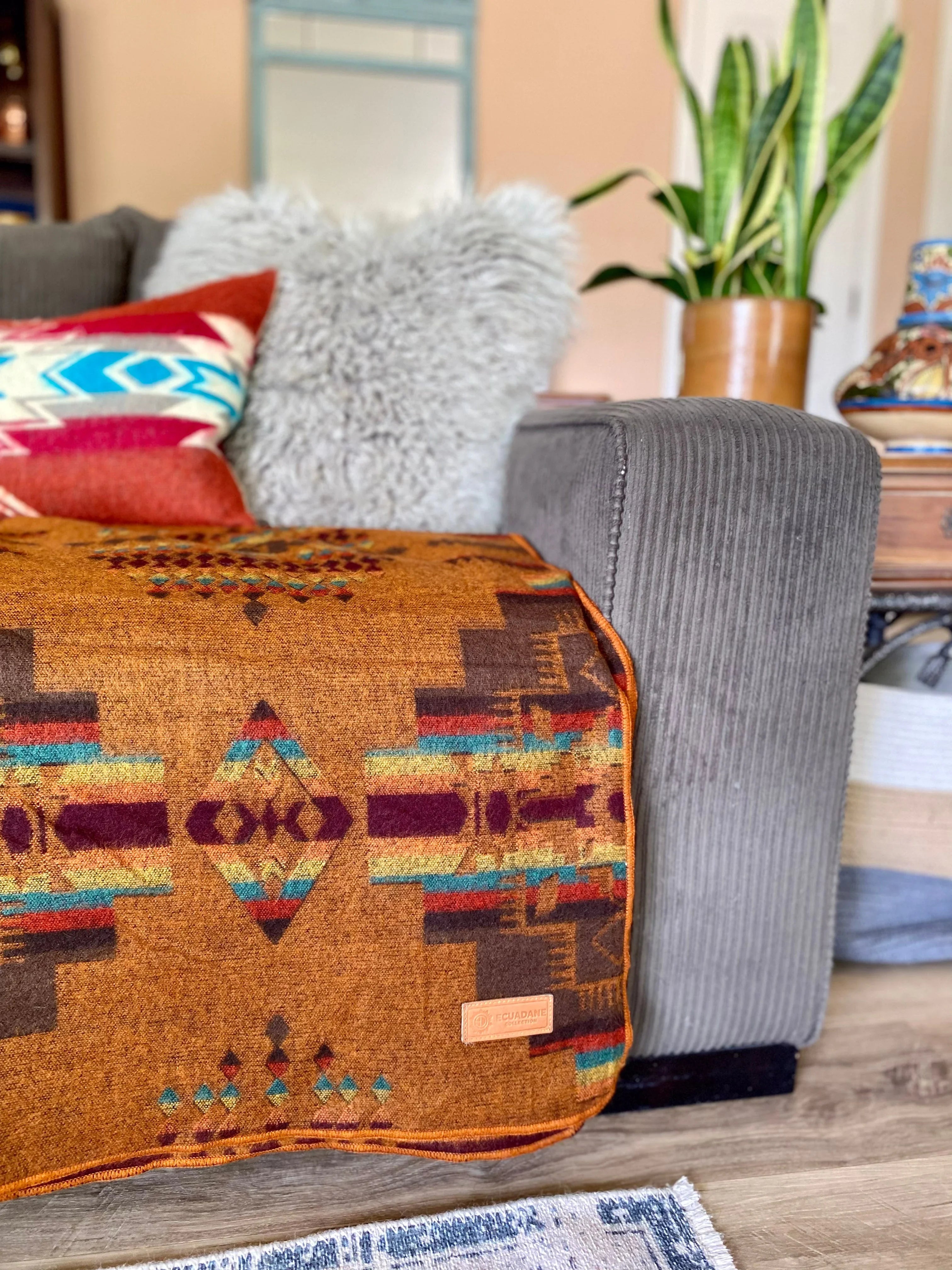 A Southwestern patterned blanket in brown, red, and blue, displayed on a couch with other cushions and a plant in the background - Your Western Decor