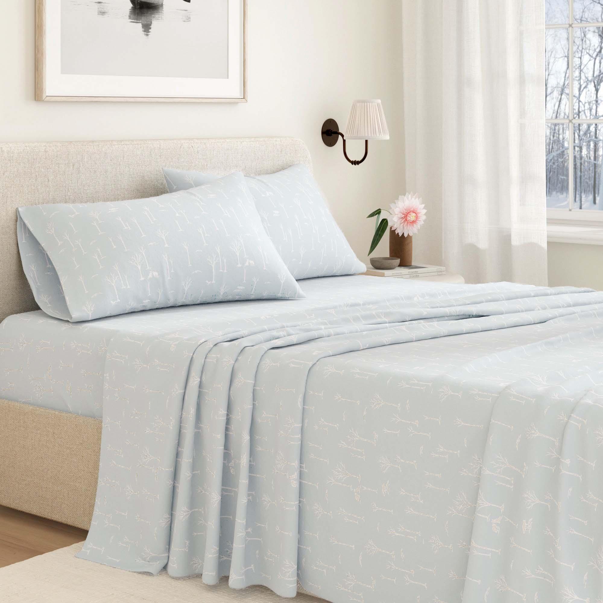Light blue branch design bedding set on a bed in a bedroom with a lamp and window in the background.