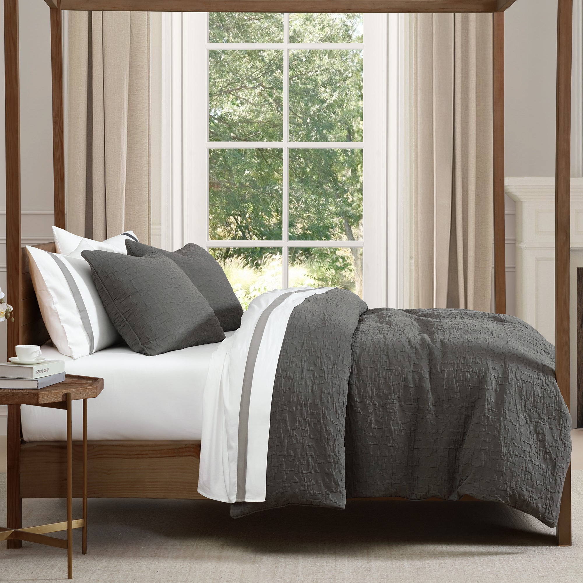 Bed with gray bedding and pillows in a room with a large window.