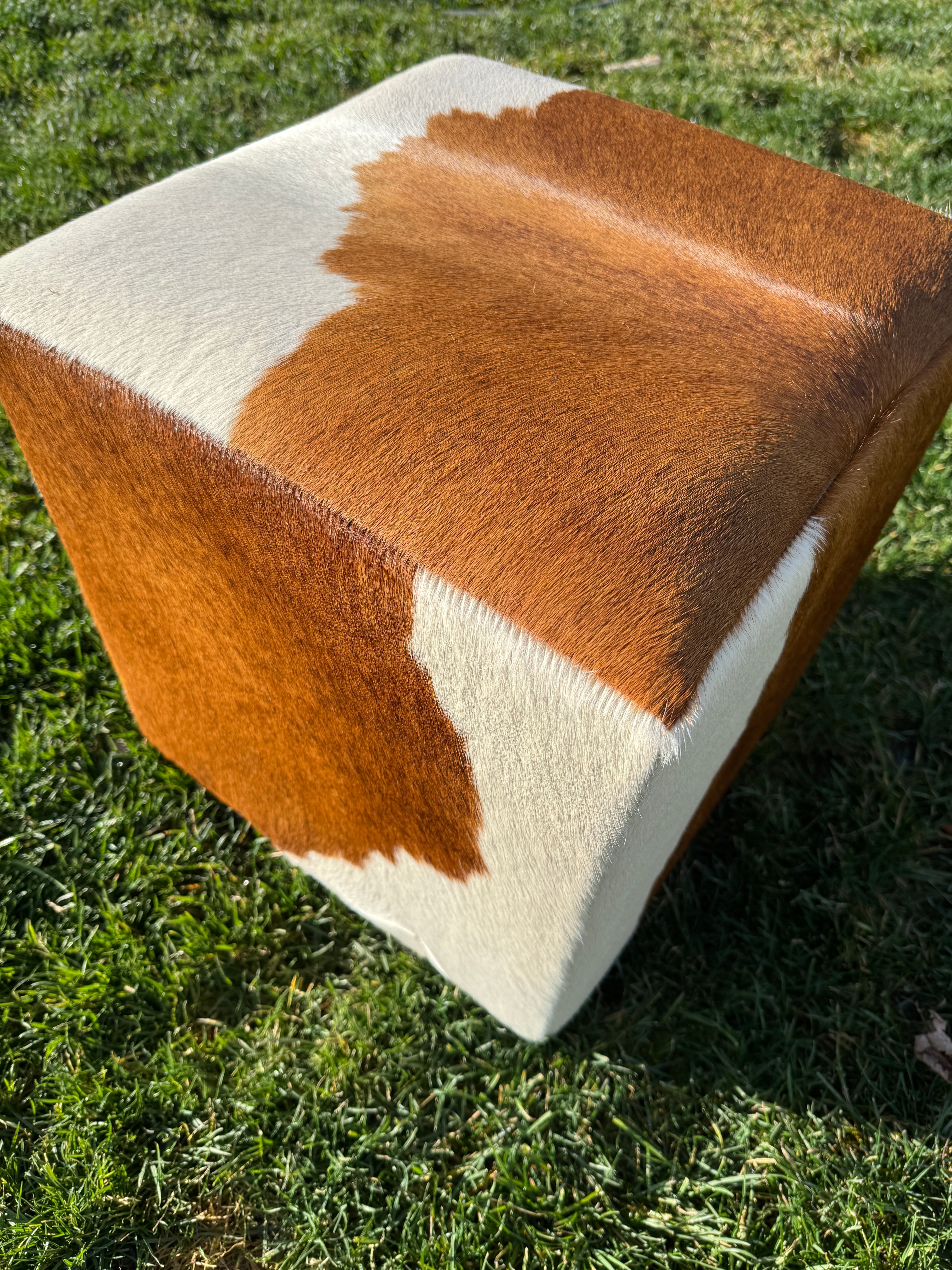 Close-up of a brown and white cowhide cube ottoman / footstool on grass