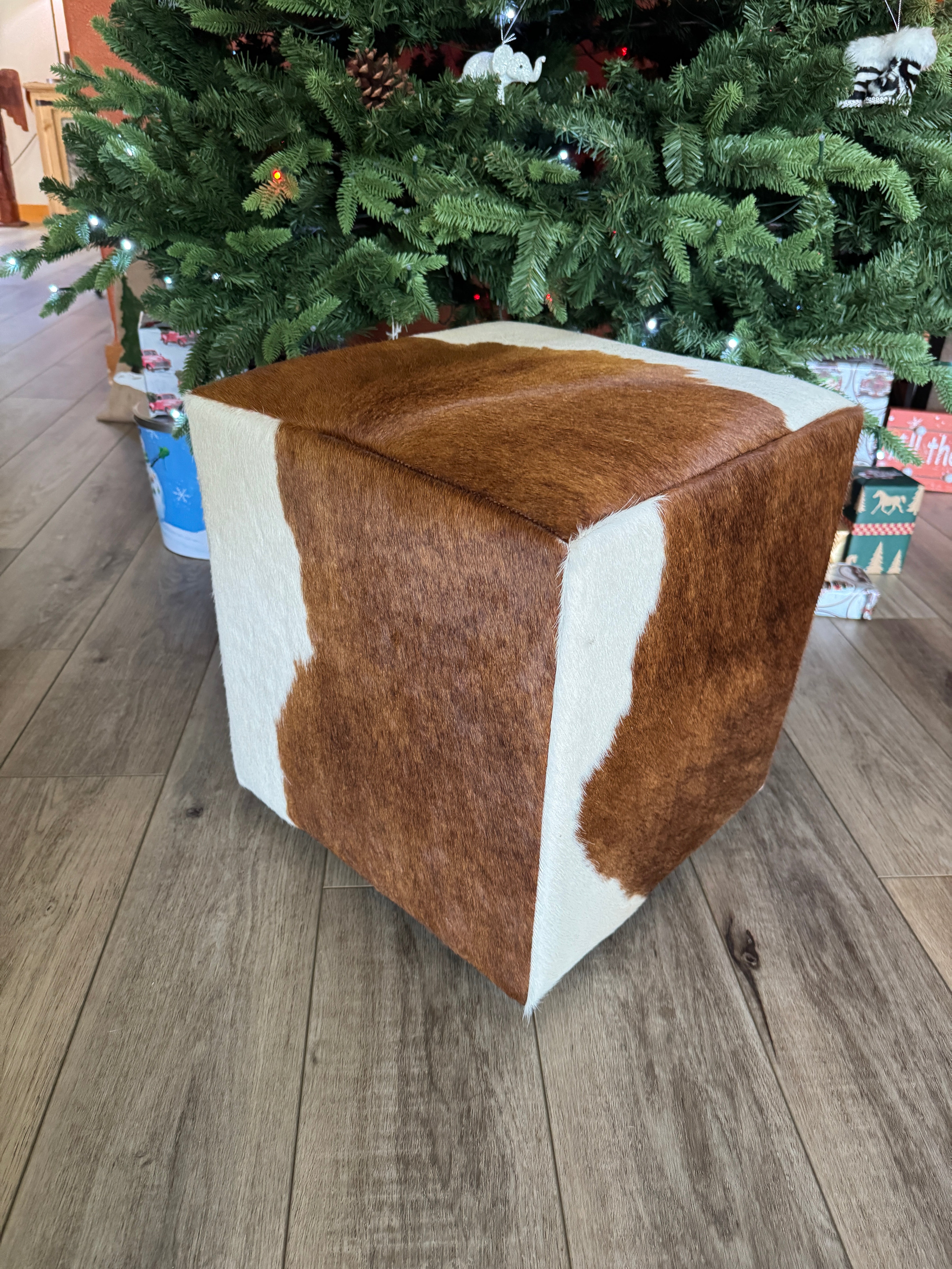 Brown and white cowhide cube ottoman on feet in front of Christmas tree, with natural hide pattern in Western rustic, yet elegant style