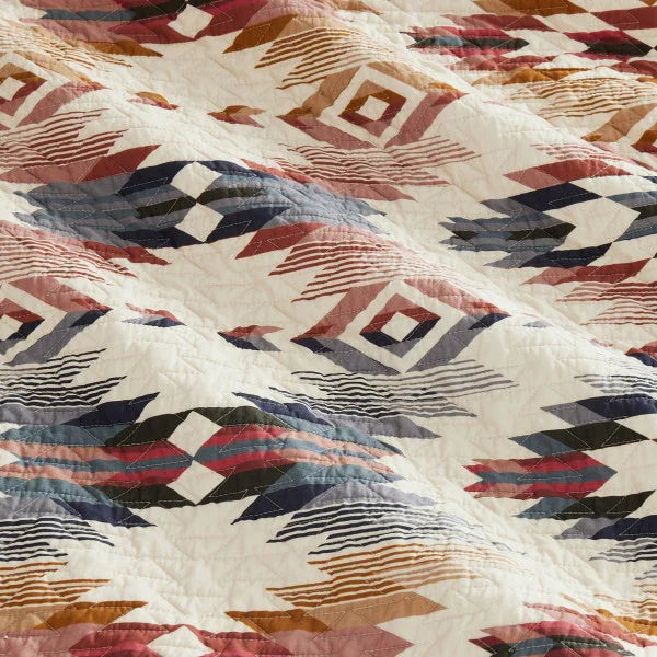 Close-up of a quilt with geometric pattern in red, blue, and brown on a white background