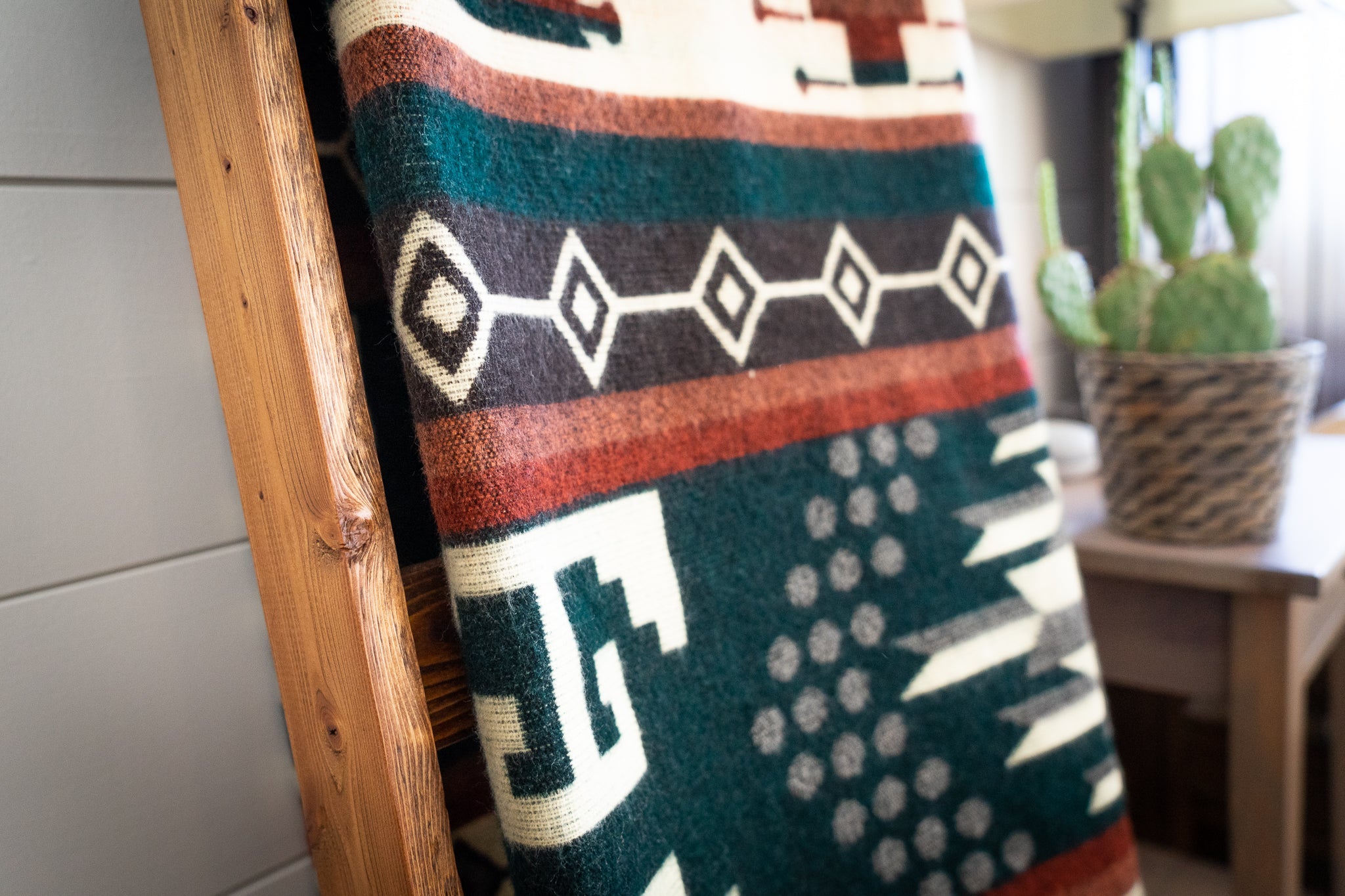 Decorative Alpaca blanket with geometric pattern on a wooden ladder, brown leather chair, and small table with lamp and cactus.