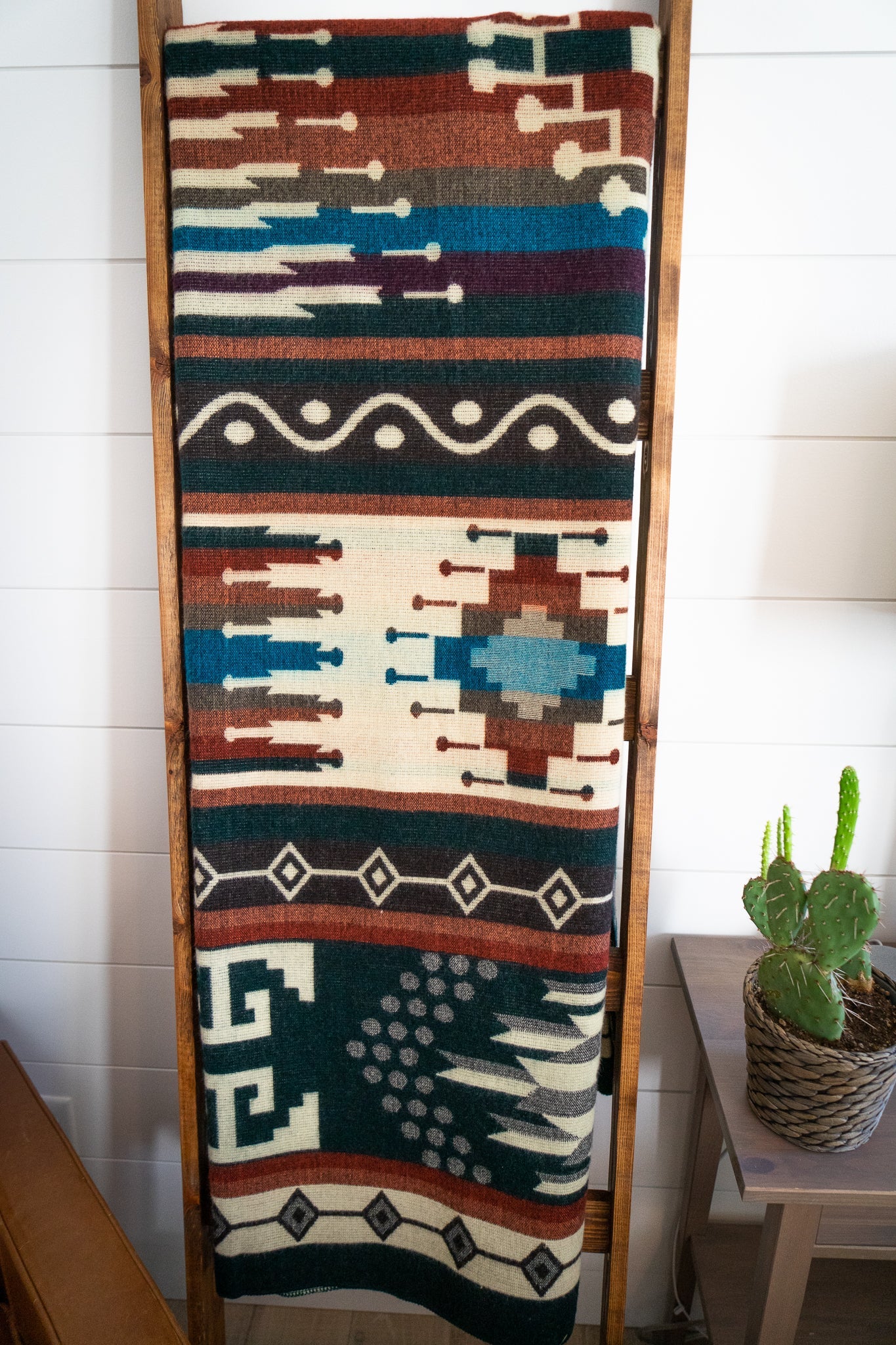 Decorative Alpaca blanket with geometric pattern on a wooden ladder, brown leather chair, and small table with lamp and cactus.