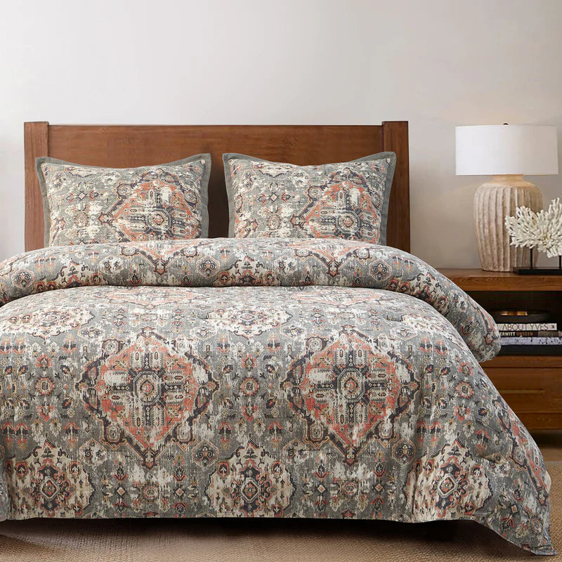 Patterned bedding set in grays, salmon and ivory on a a bed with a wooden headboard and nightstand.
