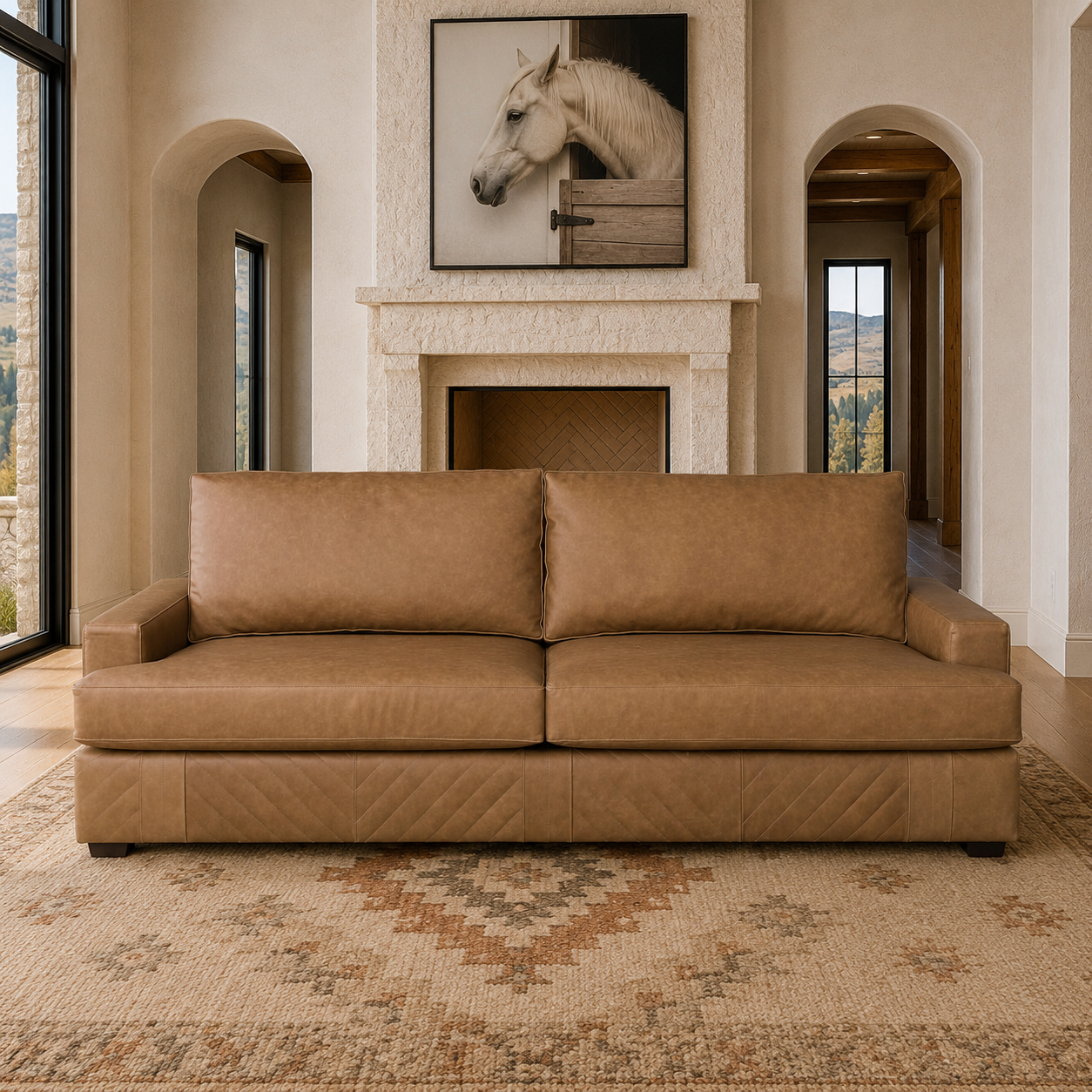 A tan leather two-seater sofa with diamond-quilted paneling on the base, set in a modern, warm-toned living room with a patterned rug, canvas horse art, stone fireplace, and arched windows.