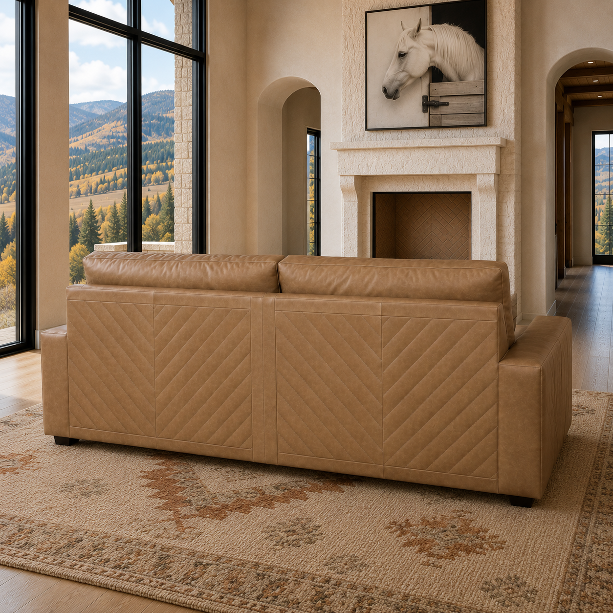 A tan quilted chevron pattern leather sofa in a luxurious modern living room with a fireplace, canvas horse art, large windows showing a mountain view, and a patterned rug.