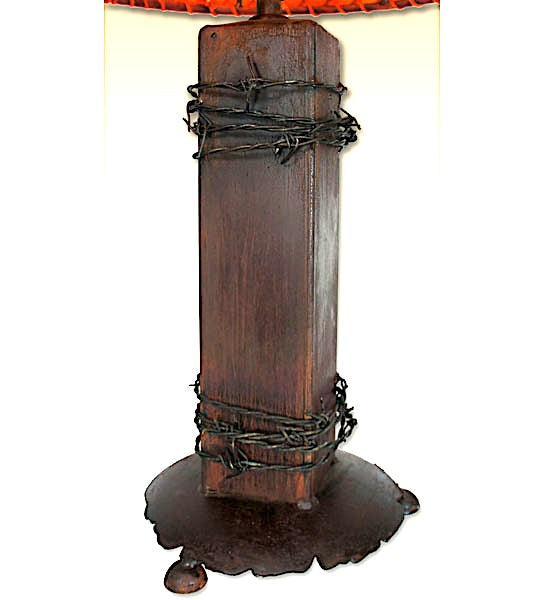 A rustic dark brown wooden table lamp featuring a thick rectangular post wrapped with black barbed wire, a matching dark metal base with a dripping effect, and a red-orange fabric shade partially visible at the top.