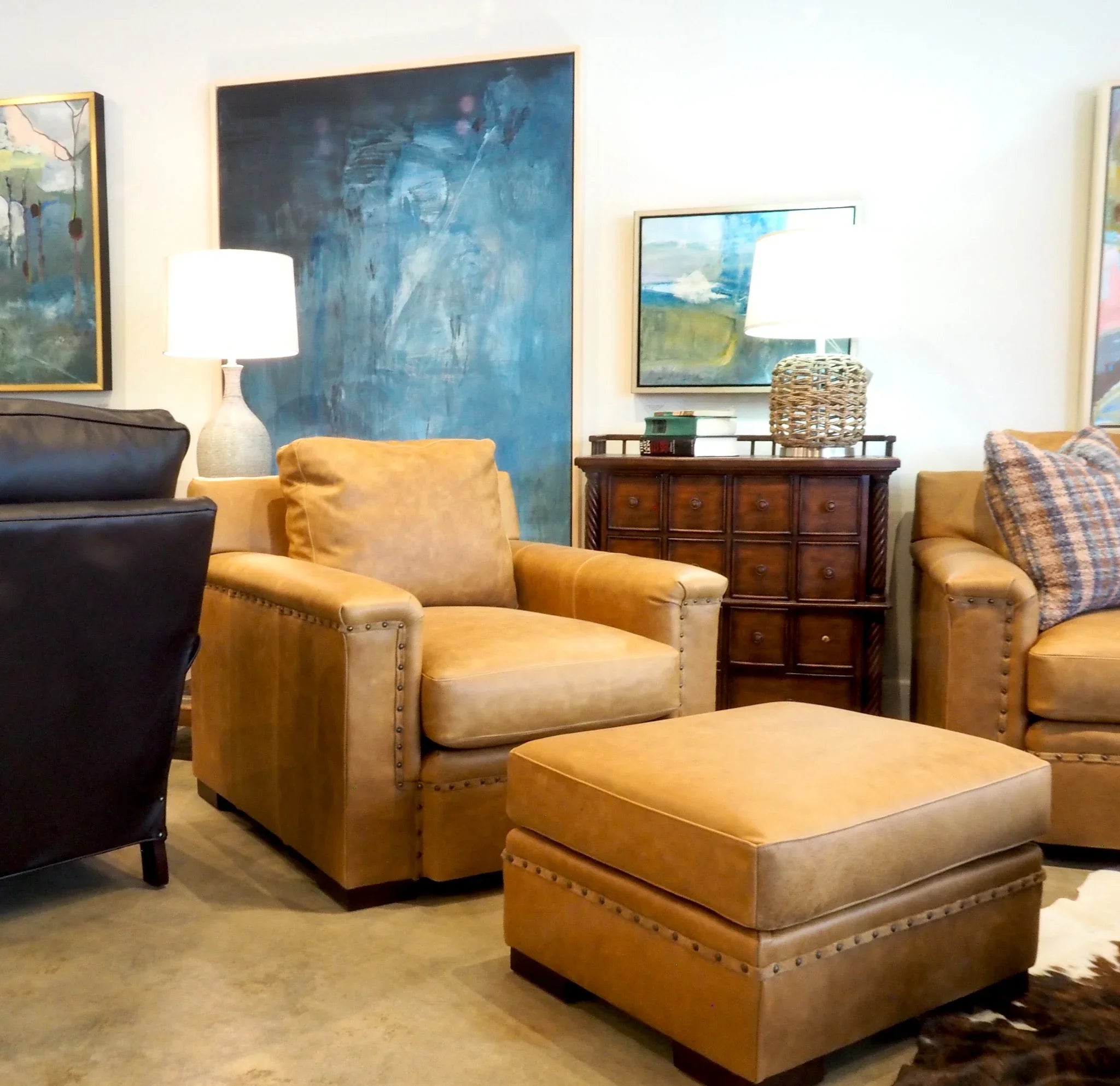 Living room with brown armchair, ottoman, and black cabinet against a wall with abstract paintings - Your Western Decor