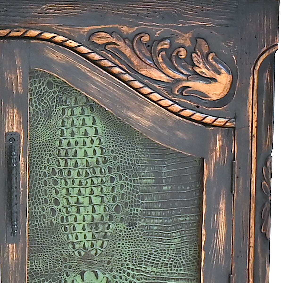 Close-up of an ornate carved wooden cabinet door with a textured green reptile-pattern glass insert and a rope detail across the top.