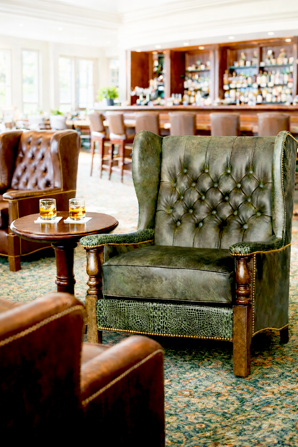 Vintage-style tufted green leather armchair in a bar setting with a wooden table and bar in the background - Your Western Decor