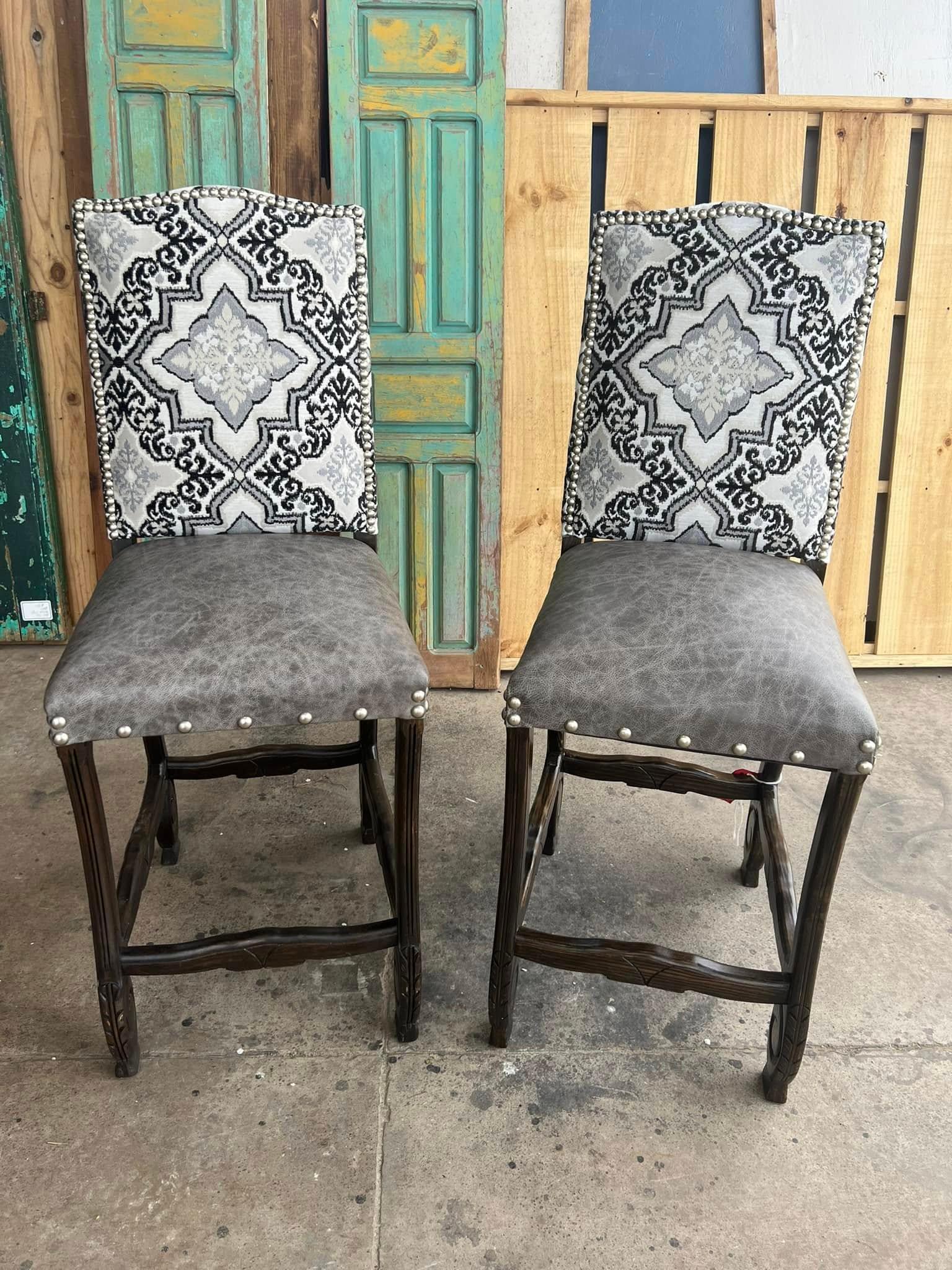 Two gray chairs with patterned backrests in front of a wooden and green door.