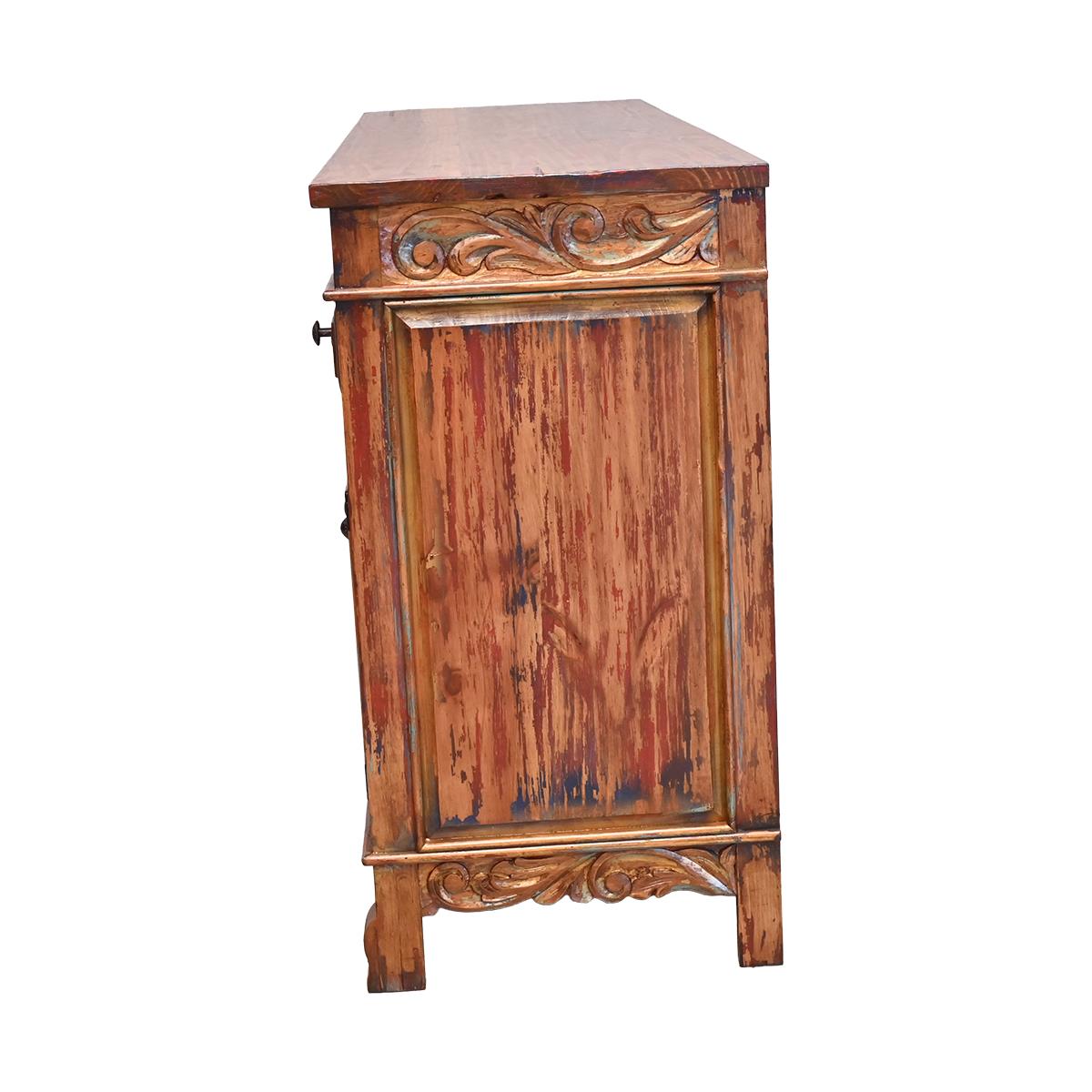 A rustic wooden cabinet with a distressed finish, featuring carved decorative details on the top and bottom, set against a plain white background.