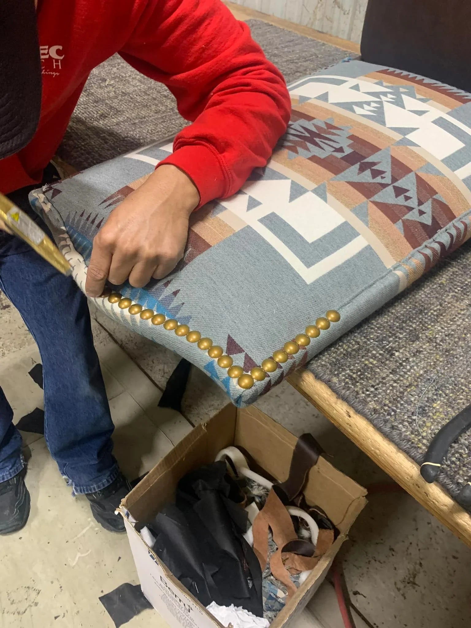 Person working on a patterned cushion with gold studs on a bench