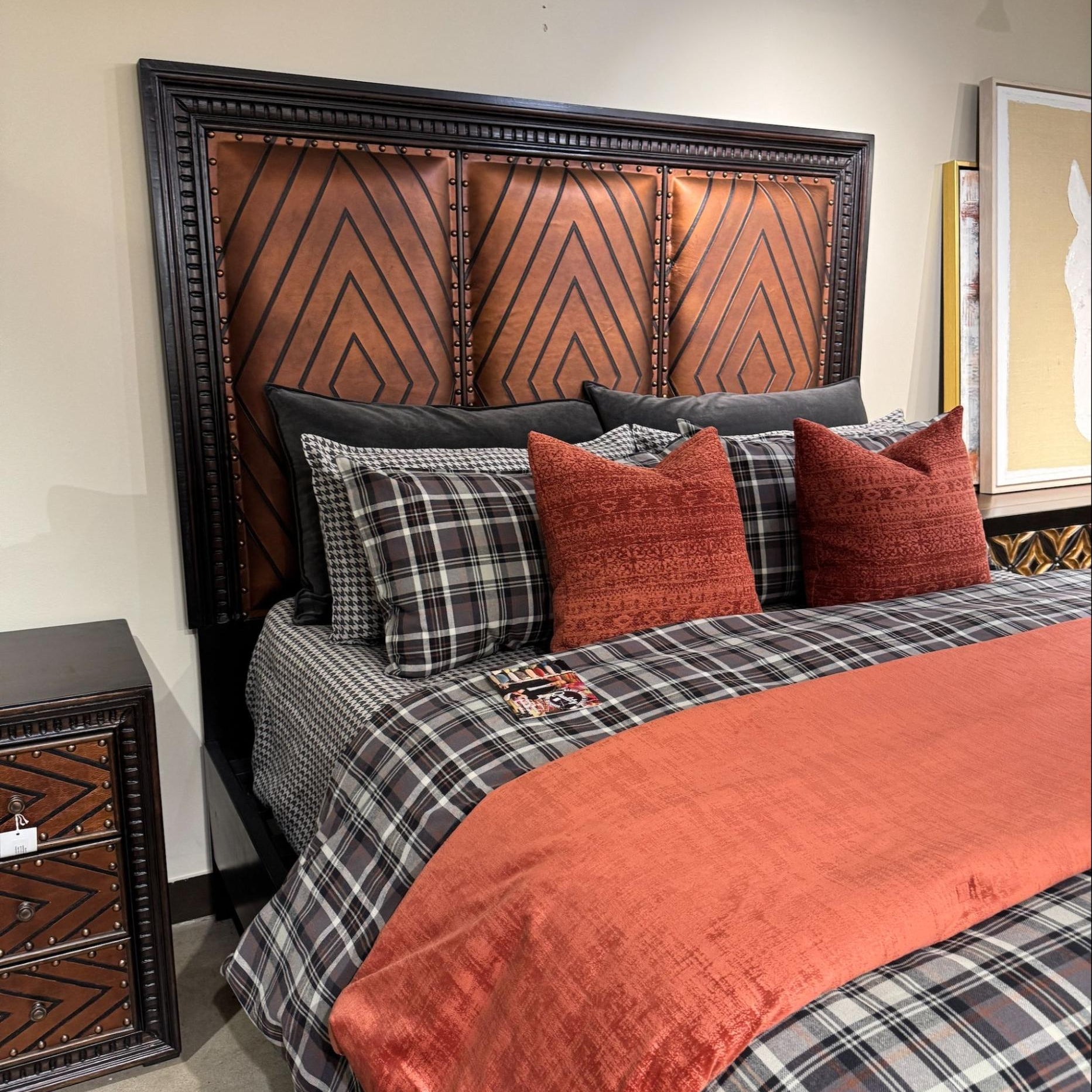 Bedroom with a bed featuring plaid bedding and red pillows, next to a wooden nightstand.