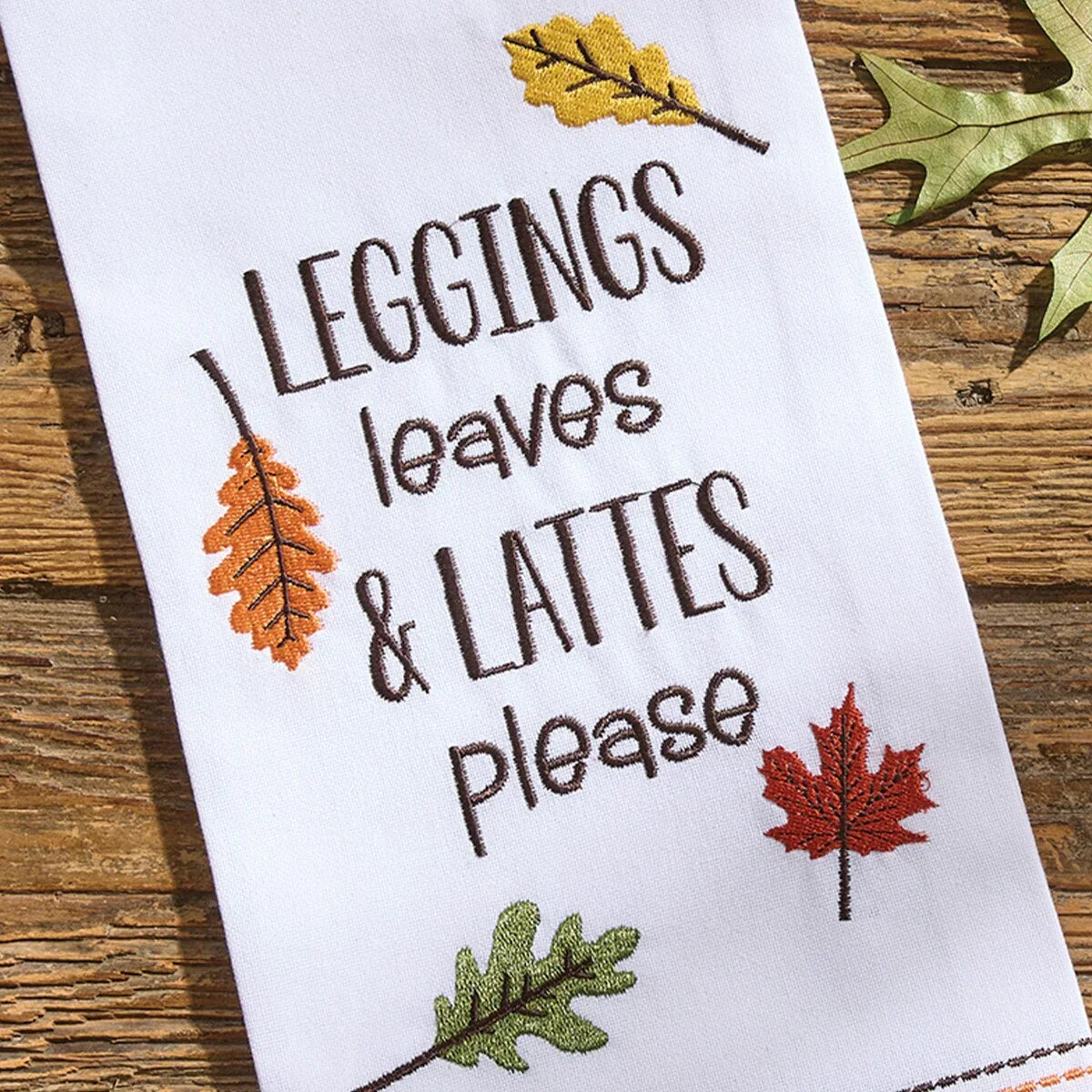 Embroidered towel with 'Leggings, leaves & lattes please' text and autumn leaves on a wooden surface - Your Western Decor