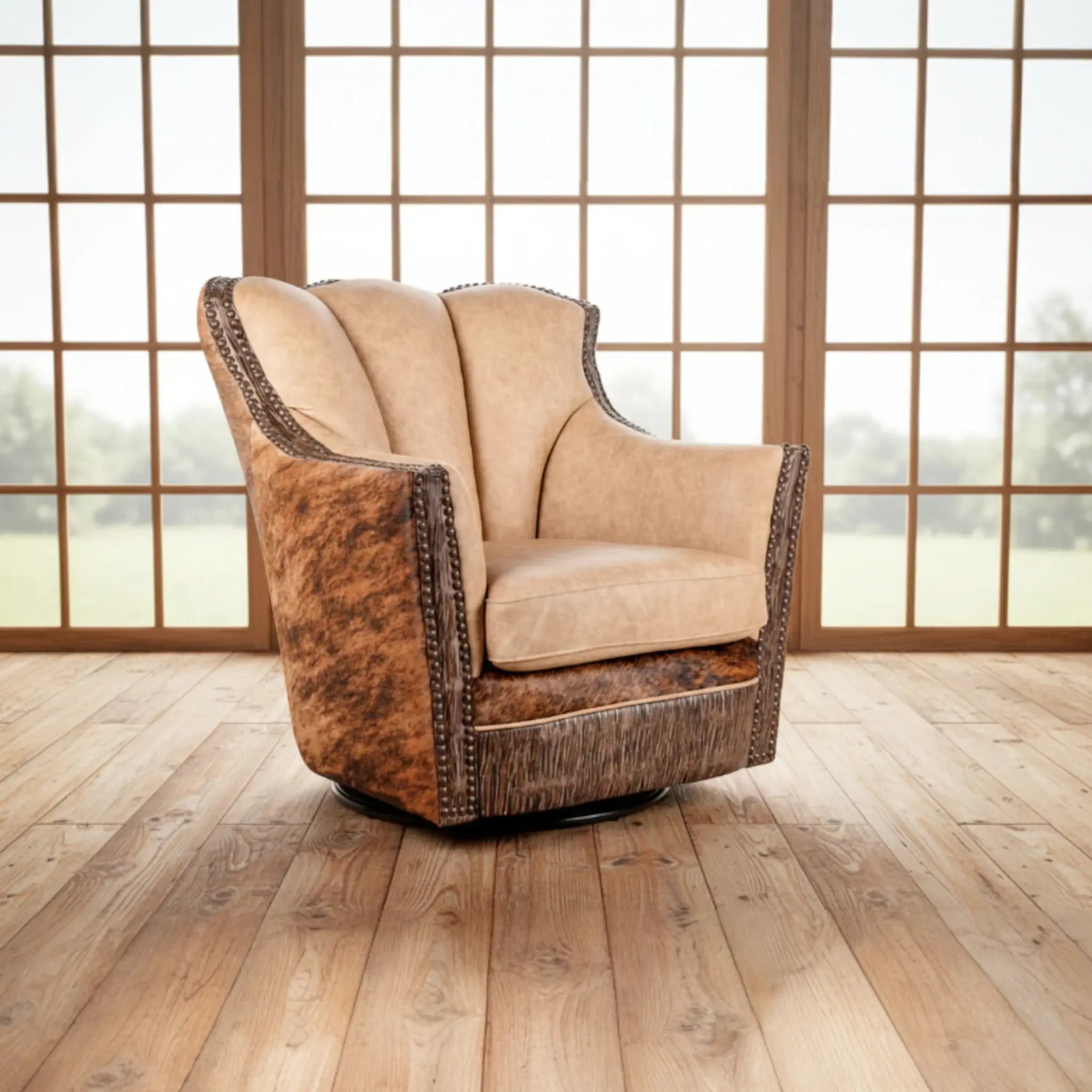 A swivel armchair with a beige suede backrest and brindle cowhide sides, featuring dark metal nailhead trim, set on a light wood floor in front of shoji-style window panels.