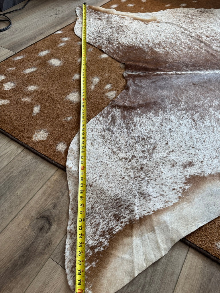 Measurement of a cowhide rug with a tape measure on a wooden floor.