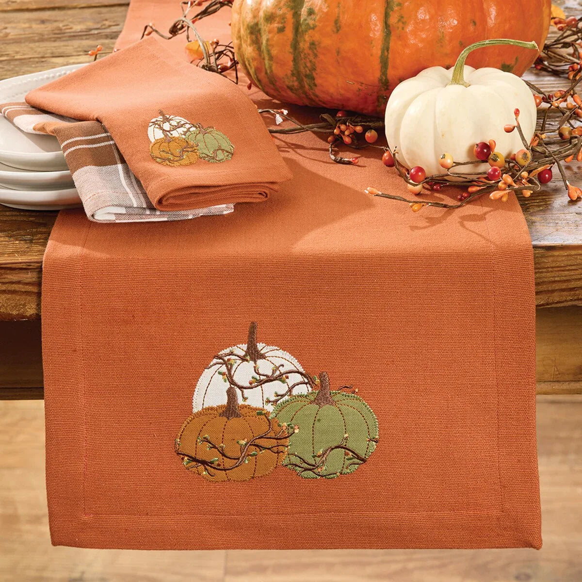 Table setting with an embroidered pumpkin design on a rust-colored table runner, surrounded by pumpkins and foliage Your Western Decor