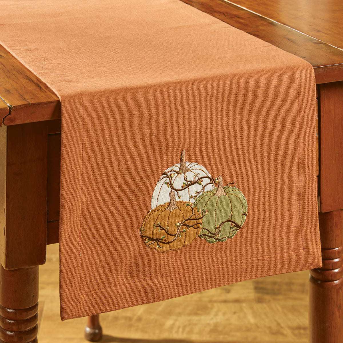 Brown table runner with embroidered pumpkins on a wooden table - Your Western Decor