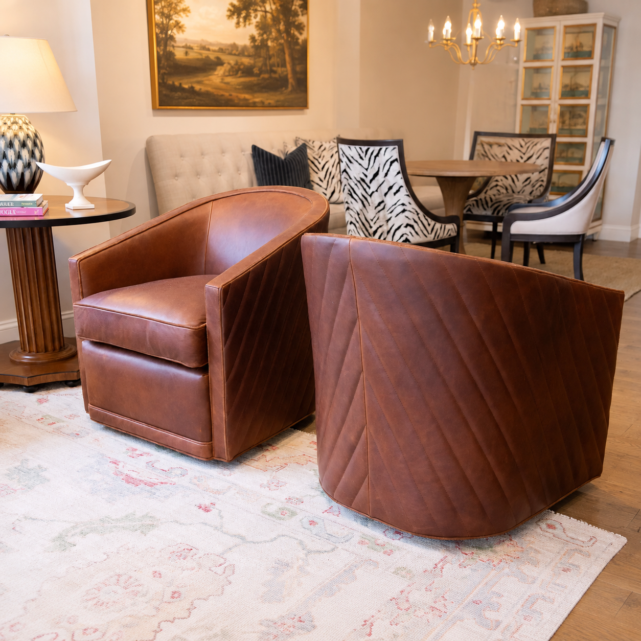 Two brown leather swivel armchairs in a styled living room setting, with one showing a curved back and the other showing a quilted front, placed on a patterned area rug.