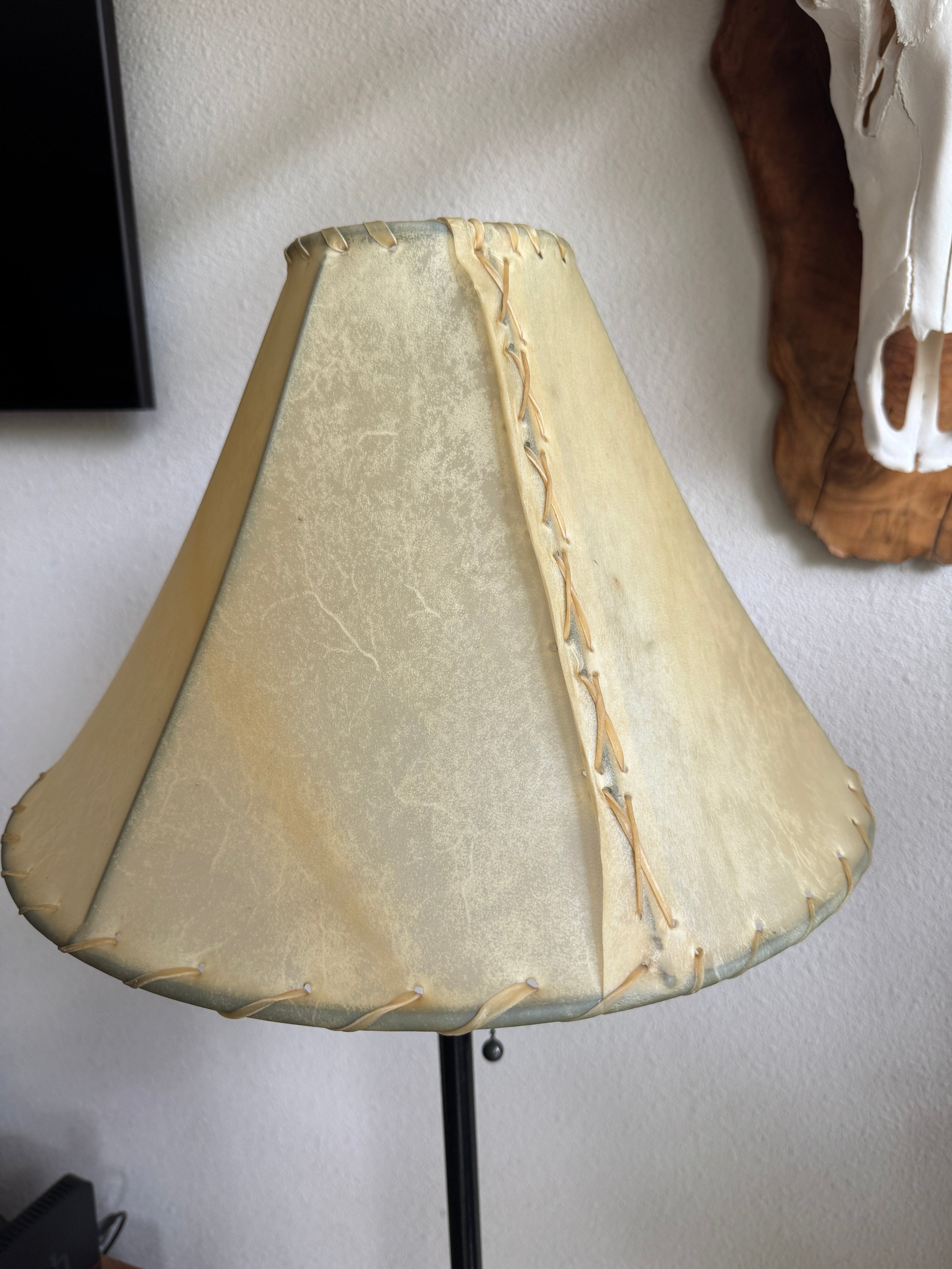 Beige rawhide lamp shade with decorative stitching on a plain wall background
