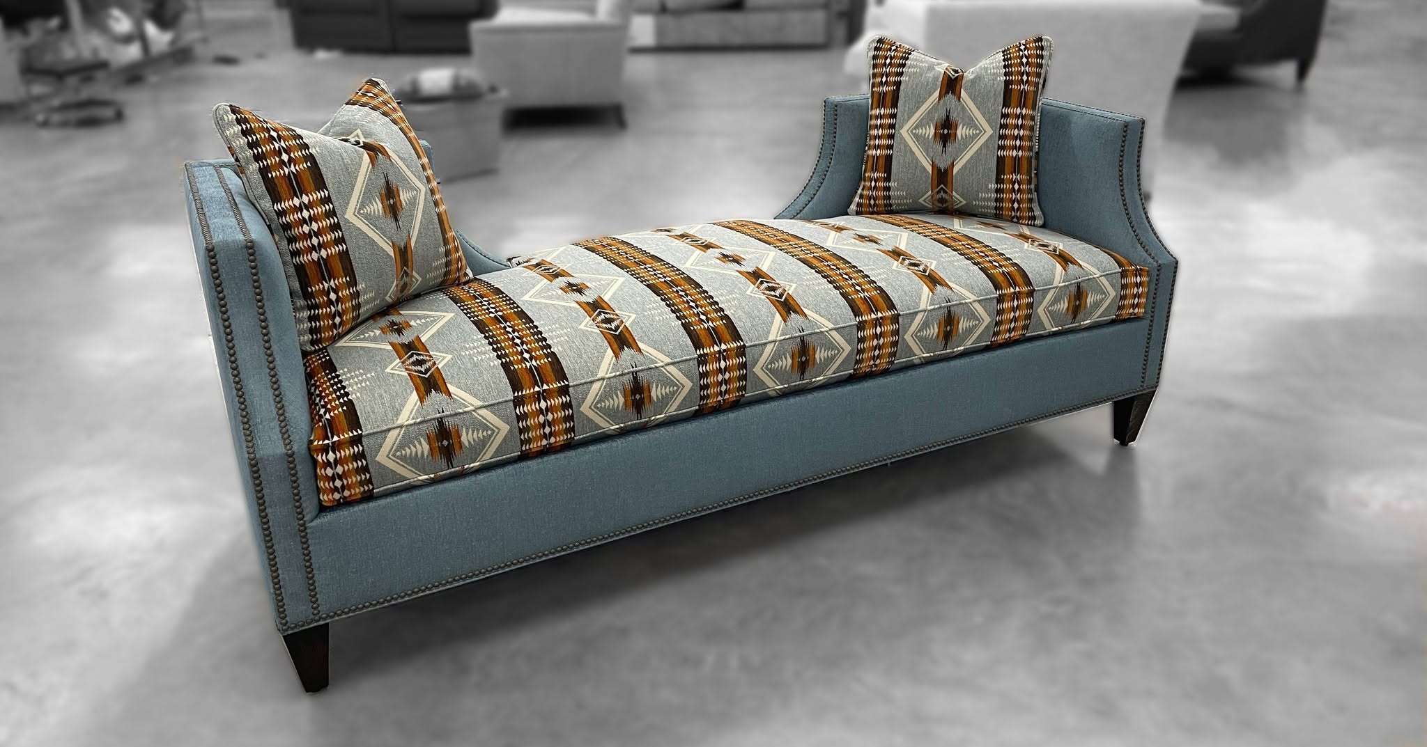 A blue upholstered chaise lounge with a patterned seat cushion and matching back cushions, shown in a modern interior setting.