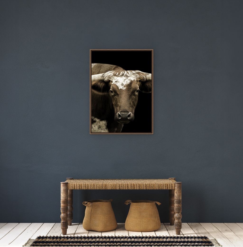 Framed artwork of a cow's face on a dark blue wall above a wooden console table with two stools - Your Western Decor