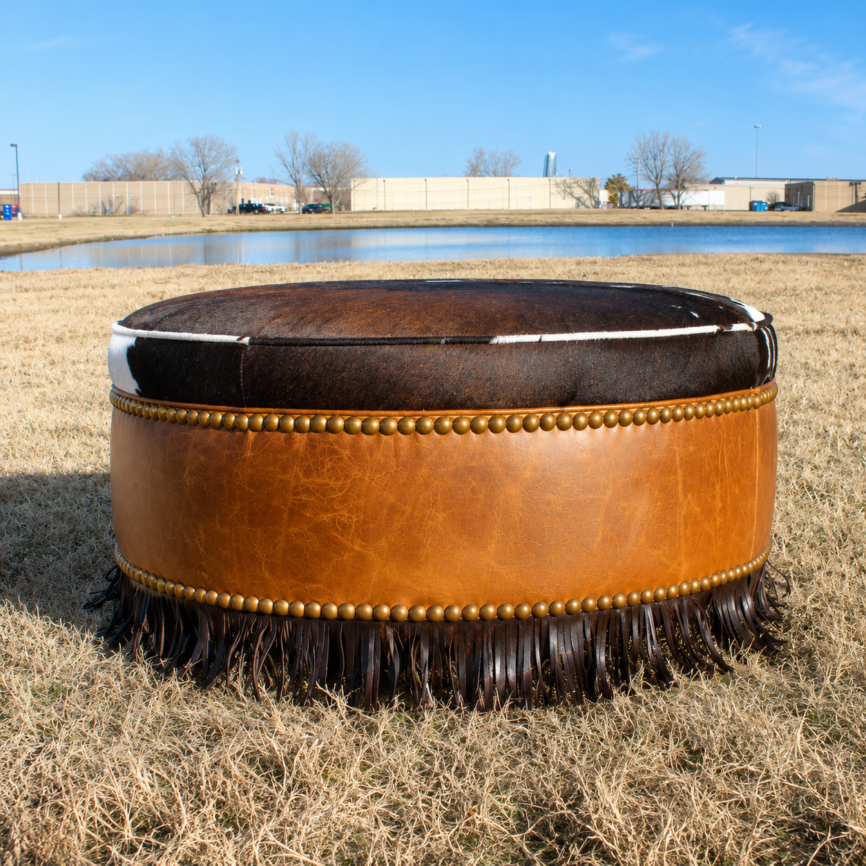 Cowhide and leather round ottoman with fringe and nail trim
