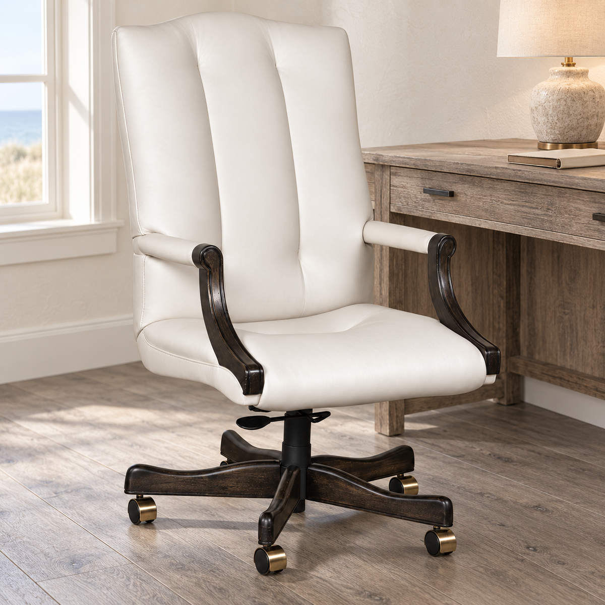 A white leather office chair with dark wood armrests and a black wheeled base, positioned in a home office setting next to a wooden desk.