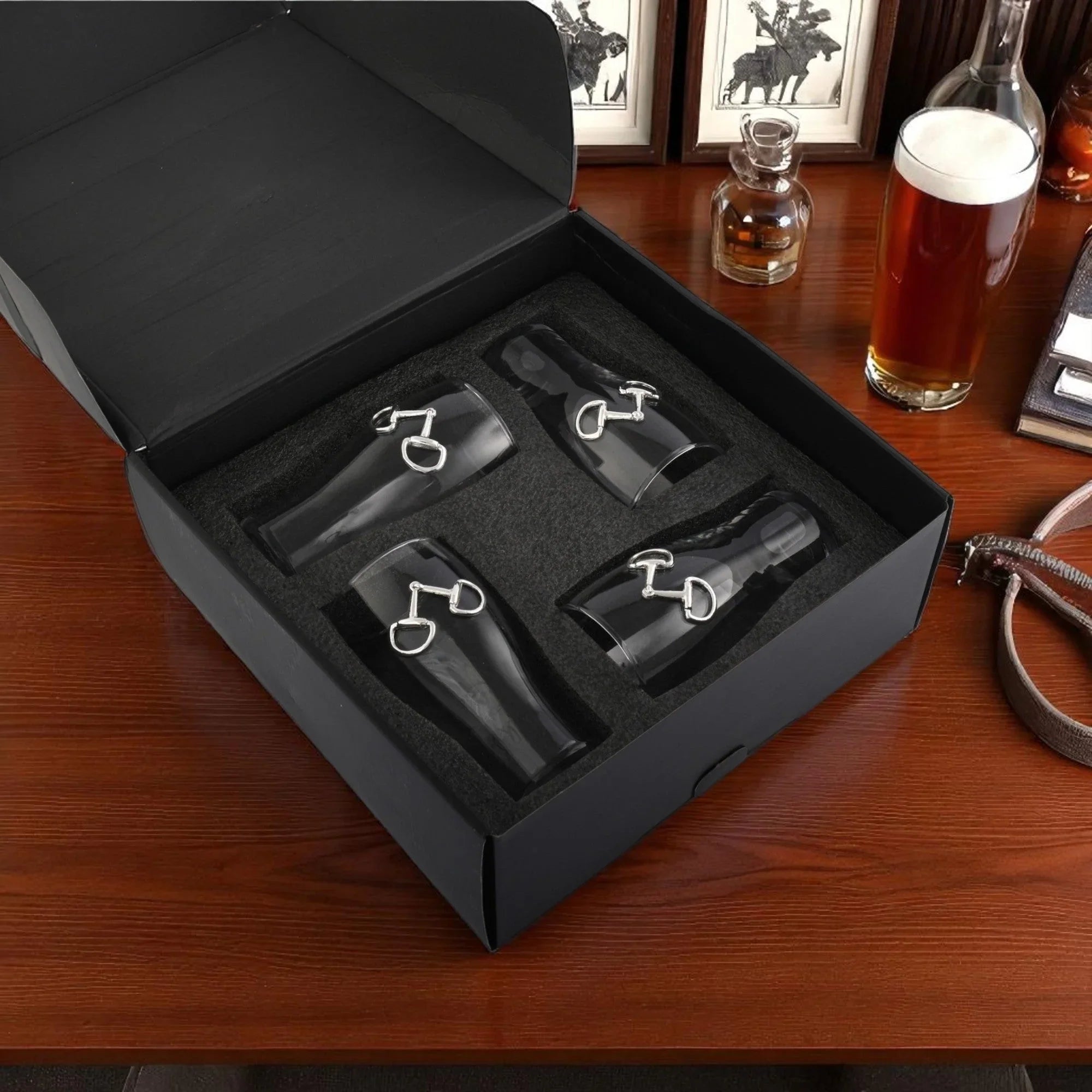 Set of four snaffle bit beer glasses in black box on a wooden table with a beer bottle and glasses in the background.