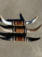 Three decorative steer horns with leather bands on a cement floor