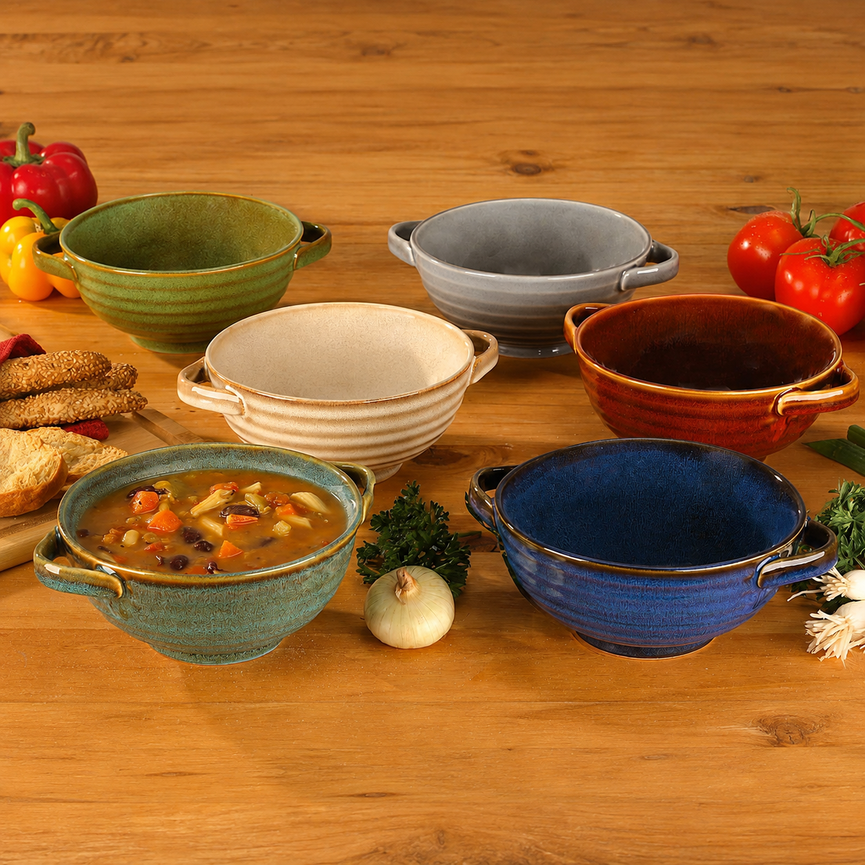 Six ceramic ribbed soup bowls with handles in assorted colors including blue, green, gray, beige, orange, and red, arranged on a wooden table with food props like vegetables, bread, and a bowl of soup.