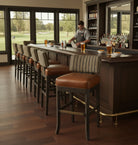 Bar with wooden counter and leather stools, bartender preparing drinks, large windows overlooking a golf course - Your Western Decor