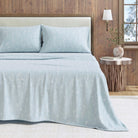 Light blue bedding set on a bed with a wooden headboard and side table in a room.
