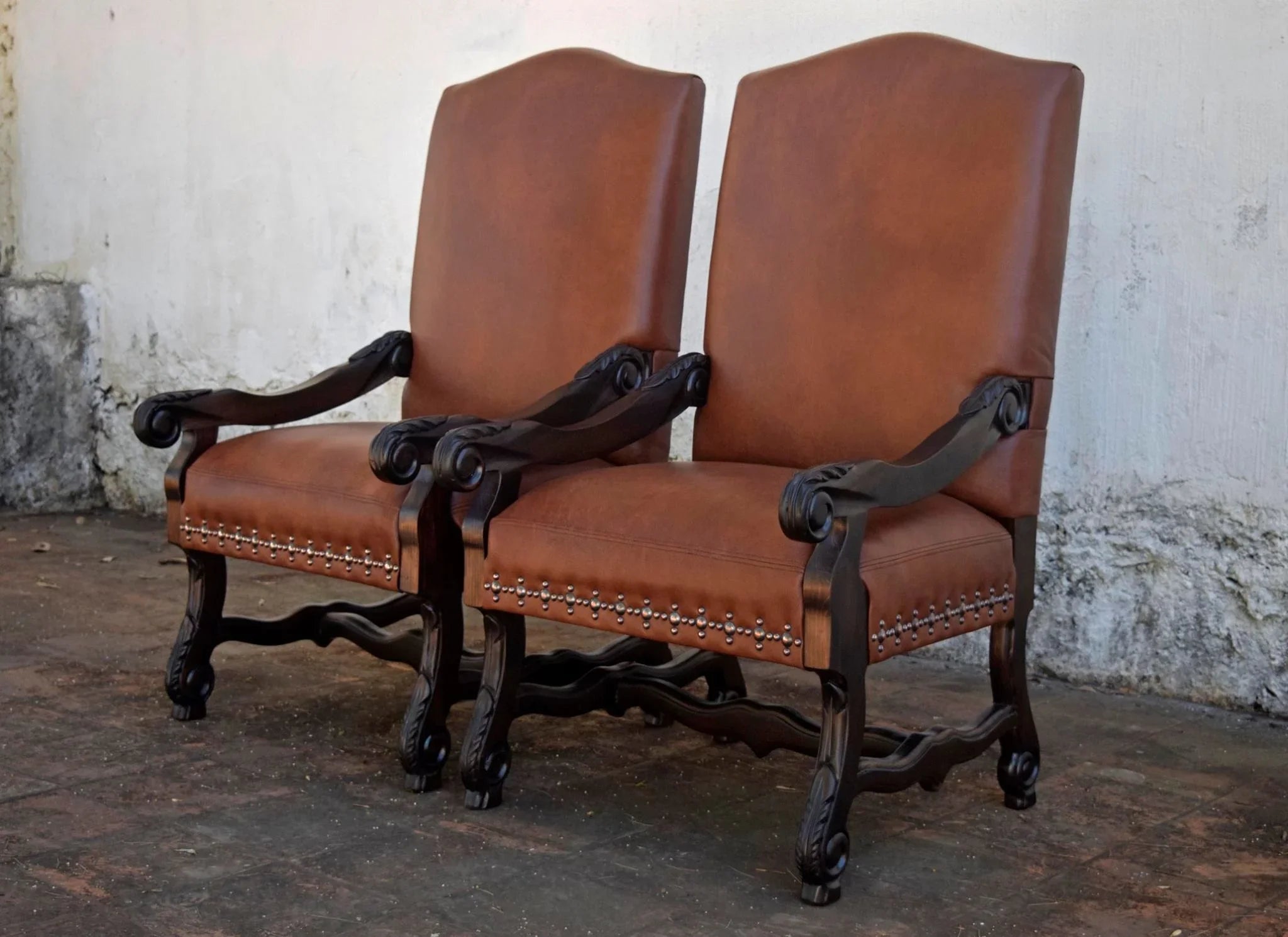 Pair of brown leather chairs with ornate wooden frames against a textured wall.