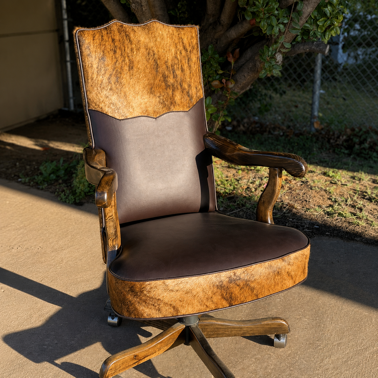 A high-back swivel office chair with a mix of brown leather and textured animal-hide upholstery, set outdoors on a concrete surface.