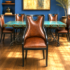 A dining room scene showing a brown leather high-back chair in the foreground, with matching brown leather and turquoise table chairs around a rectangular table with a turquoise top and black wrought-iron legs. Blue wall, wood floor, shelving, and wall art are visible.