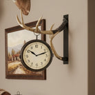 Wall clock with deer antlers mounted on a wall next to a framed picture.