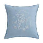 A square light blue throw pillow featuring a white embroidered illustration of a cowboy riding a horse with cacti and arches.