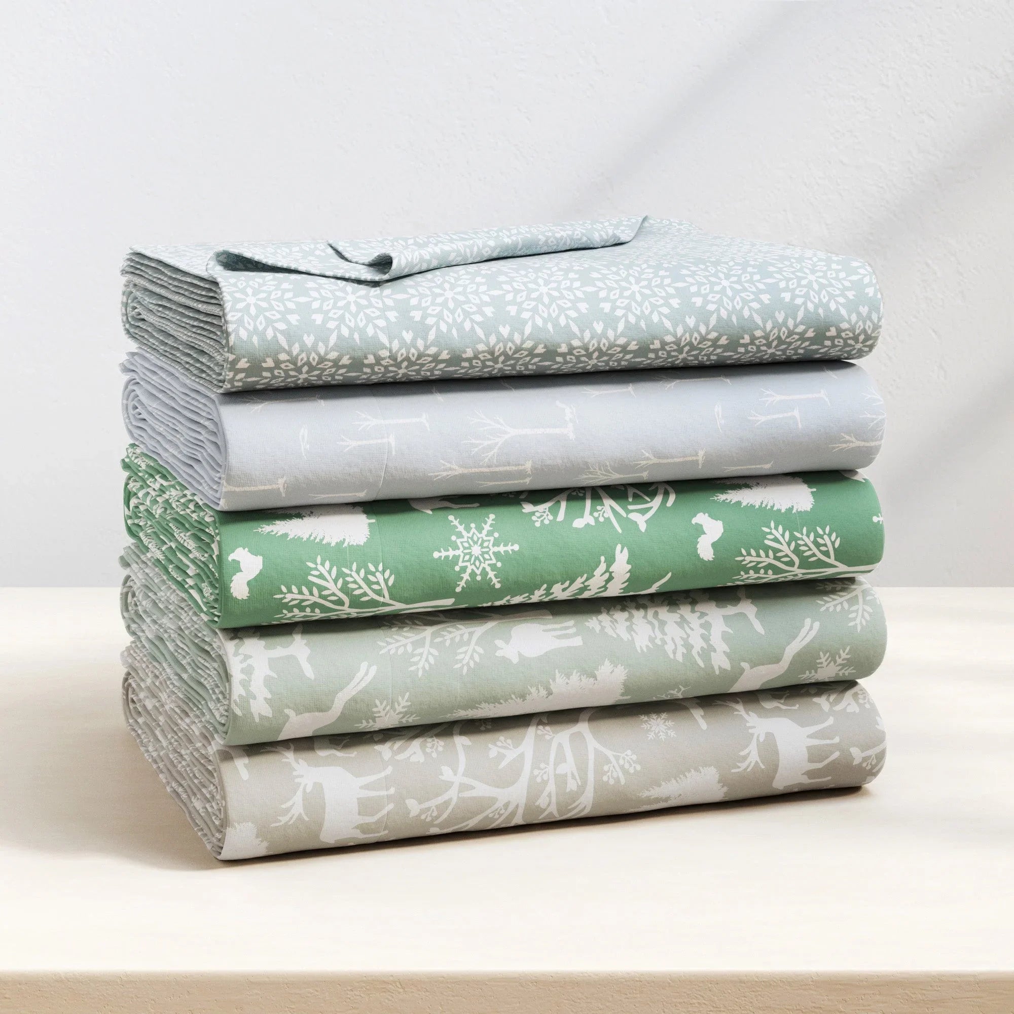 Stack of folded fabric sheets with nature-themed patterns on a white surface.