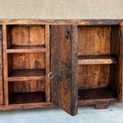 A rustic wooden sideboard cabinet with an open door, showing three interior shelves on the left and one larger shelf on the right. The cabinet has a distressed dark brown finish with blackened wood grain and an antique metal latch on the door.