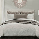 Neatly made bed with gray bedding and decorative pillows in a bedroom setting.
