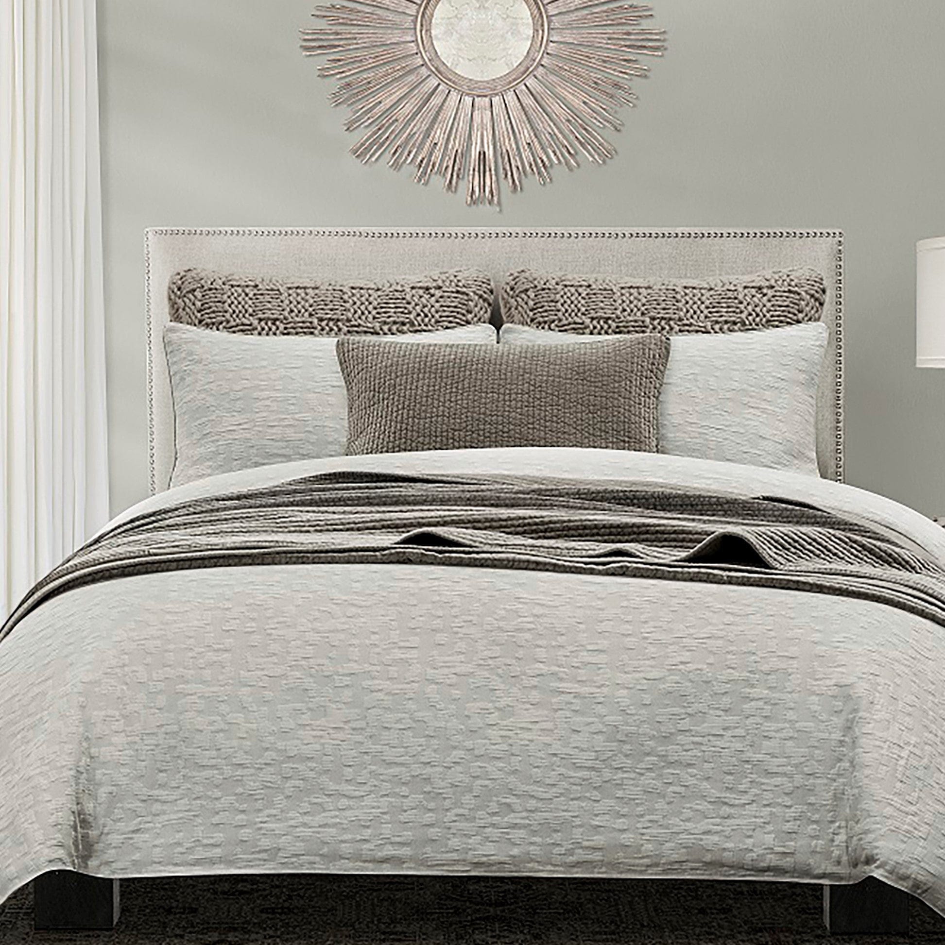 Neatly made bed with gray bedding and decorative pillows in a bedroom setting.