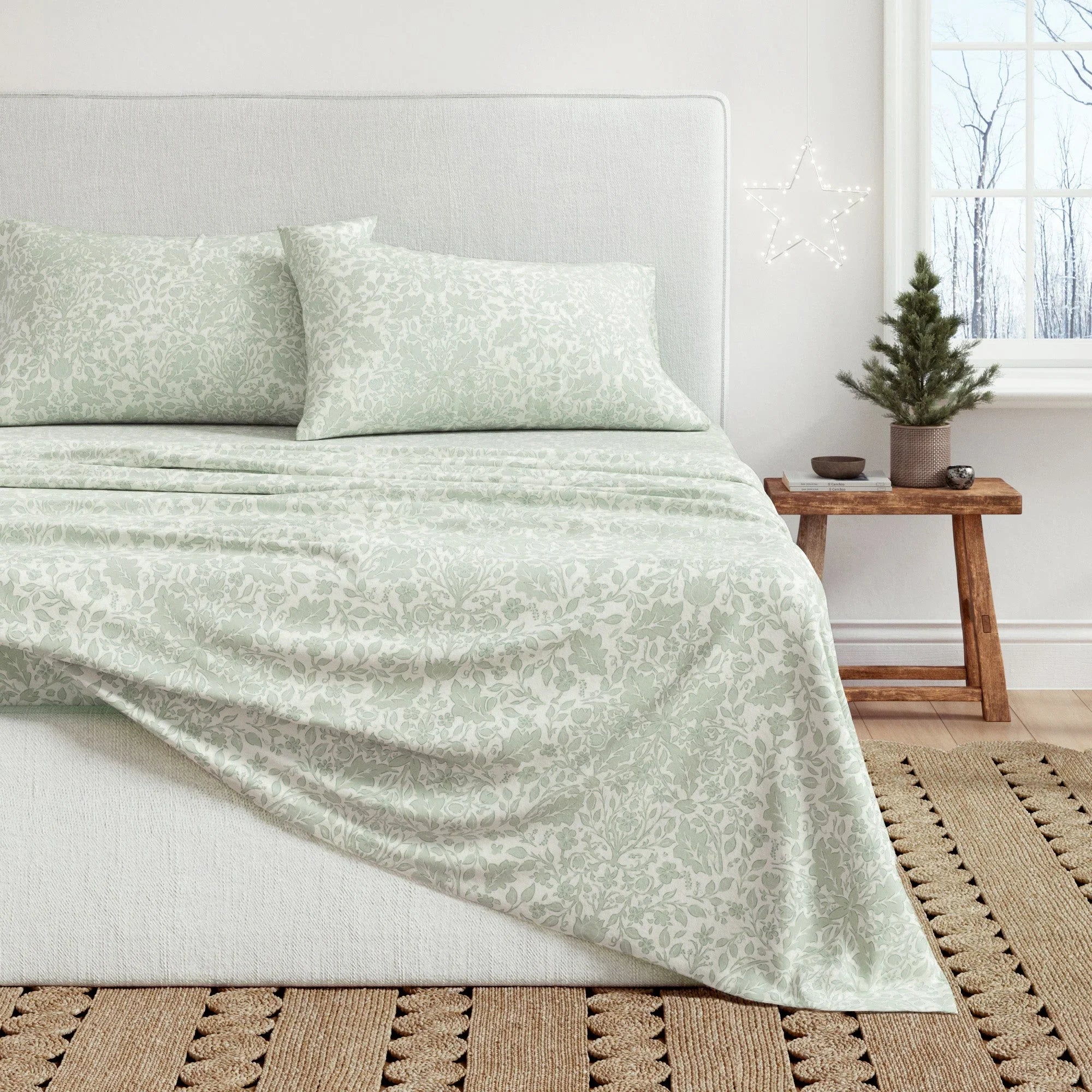 Bed with light green floral-patterned bedding in a room with a small Christmas tree.
