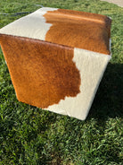 cowhide ottoman on grass in brown and white hide