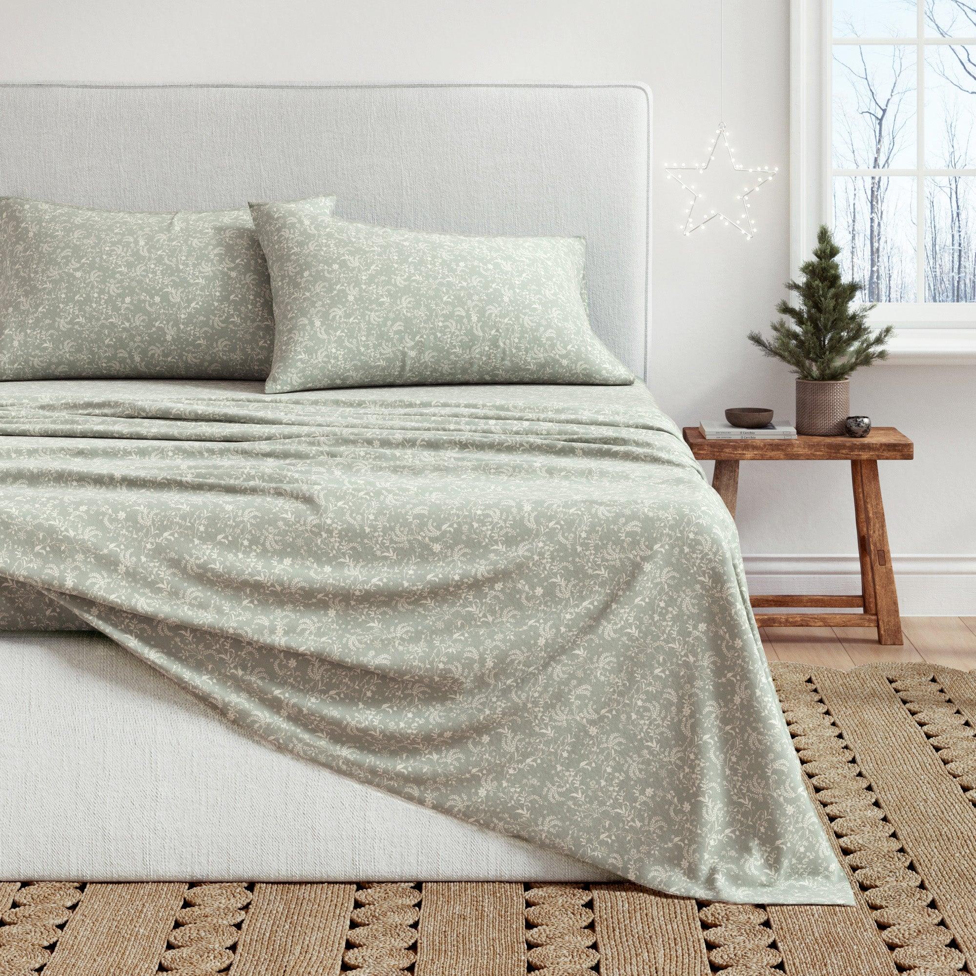 Bed with light green bedding in a room with a small Christmas tree.