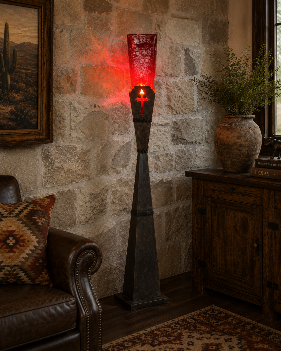 A tall decorative floor lamp with a dark metal tapered base and a textured red glass shade, glowing with warm red light in a rustic room with a stone wall, leather chair, and wooden cabinet.