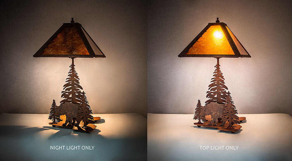 Table lamp with decorative metal pine tree and bear base, shown with night light and top light on a neutral background.
